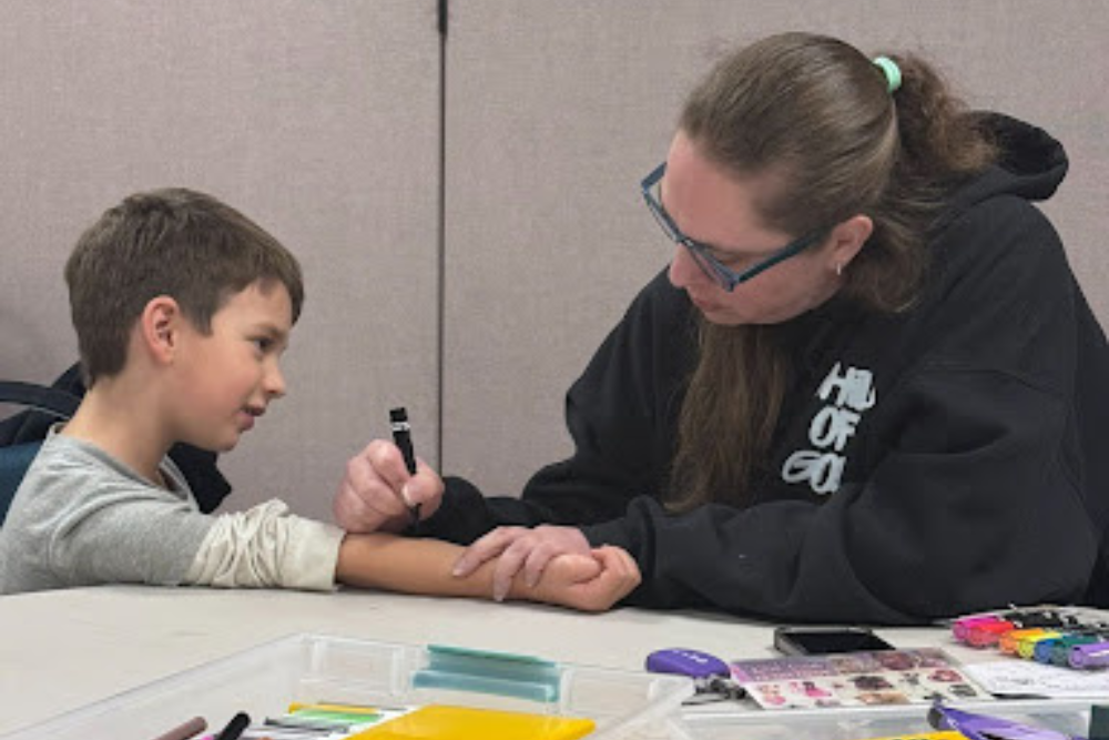 A man in black shirt is writing something into the arms of the child